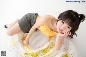 A woman in a yellow top and gray skirt laying on a white floor.