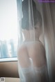 A woman in a white lingerie standing in front of a window.