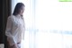 A woman in a white shirt and panties standing by a window.