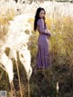 A woman in a purple dress standing in tall grass.