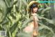 A naked woman in a straw hat standing in a corn field.