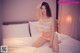 A woman in a white lingerie sitting on a bed.
